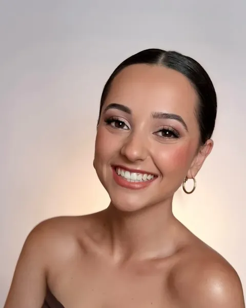 Mujer sonriendo con el pelo recogido y pendientes de aro, sobre un fondo gris claro