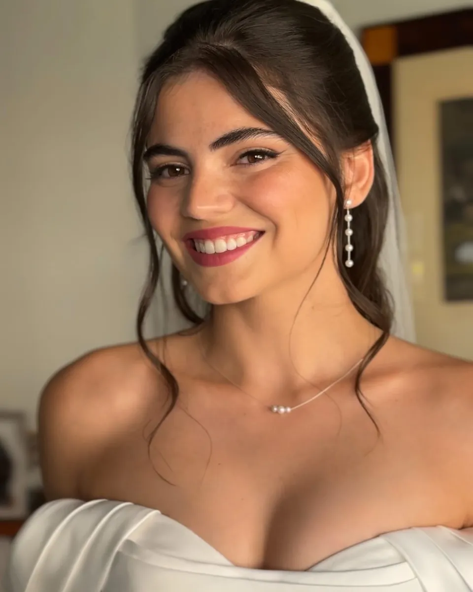 Novia morena con pendientes largos y vestido de escote barco, sonriendo